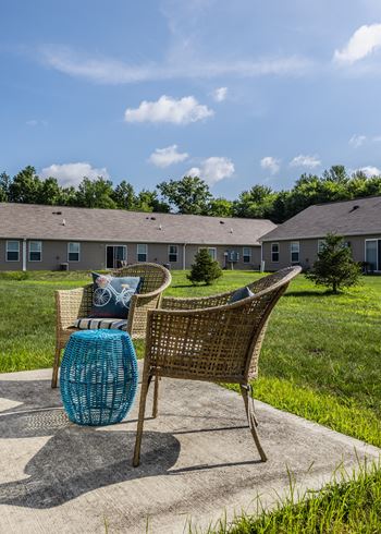 A chair with a blue cushion is placed on a concrete slab with a grassy area and a building in the background.